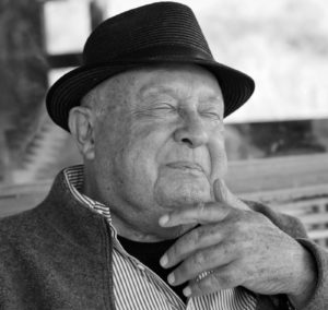 B&W photo of Robert Hall in a dapper hat with eyes closed, with a partial smile