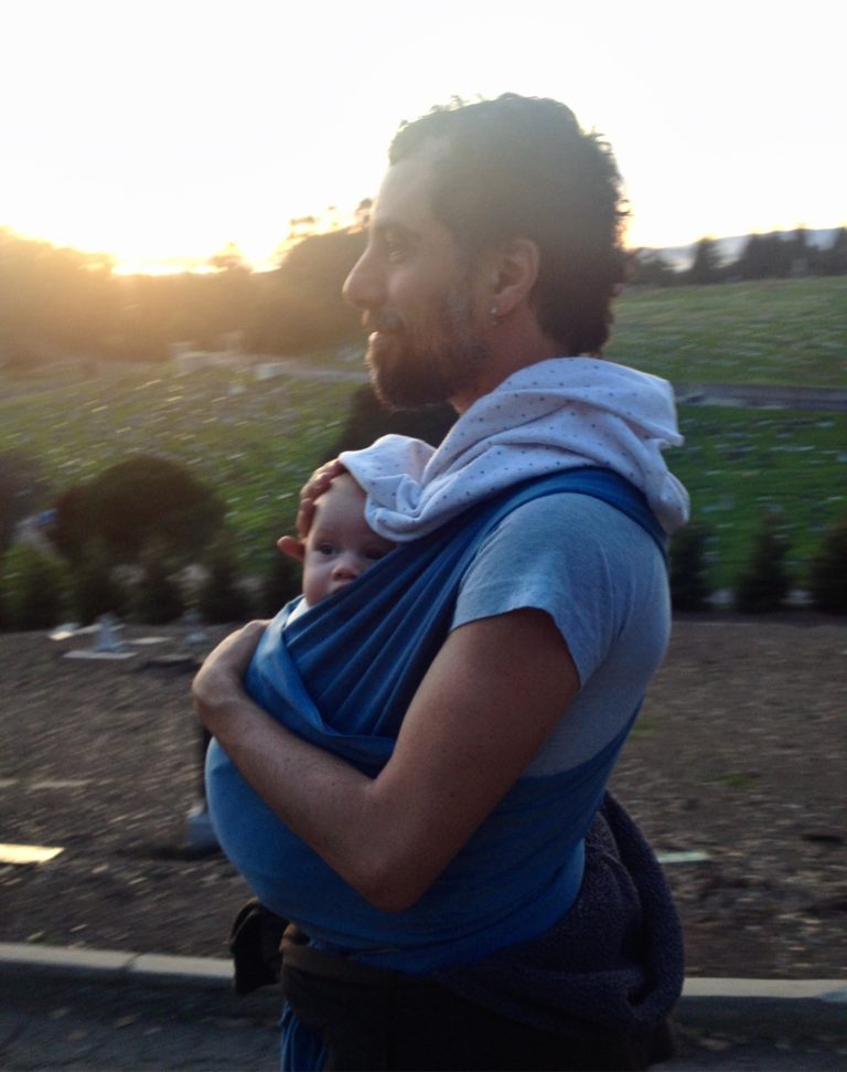 Sean outside with sunset, carrying an infant in a blue sling